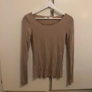 Beige ribbad långärmad topp - OANVÄND - Säljer en stilren beige ribbad topp med långa ärmar. Den har en enkel design med vågig kantdetalj vid halsen och nederkanten. Perfekt för lager-på-lager eller som den är. Helt oanvänd!