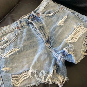 Blå jeansshorts med slitningar - Snygga blå jeansshorts med coola slitningar och fransiga kanter. Perfekta för en avslappnad stil. De har en klassisk femficksdesign och knappgylf.