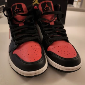 Nike Air Jordans i svart, röd och vit - Snygga Nike Air Jordans med en klassisk färgkombination av svart, röd och vit. Skorna har en hög modell med snörning och den ikoniska Air Jordan-loggan på sidan. Perfekta för dig som vill ha en stilren och sportig look.