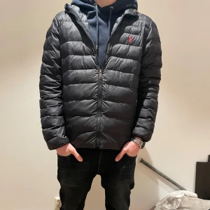 Ralph lauren jacka - Snygg svart pufferjacka från Polo Ralph Lauren med röd broderad logga på bröstet. Jackan har dragkedja och två praktiska fickor med dragkedjor. Perfekt för kyligare dagar självklart äkta skanar man qr koden kommer man till Ralph lurens hemsida köpte på nk 4200 perfekt skick 