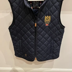 Mörkblå quiltad väst från Morris - Snygg mörkblå quiltad väst från Morris med dragkedja och broderad logotyp på bröstet. Perfekt för en stilren look. Pris kan diskuteras vid snabb affär kom med frågor 