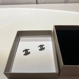 Silvriga örhängen med logotypdesign - Snygga silvriga örhängen med en elegant logotypdesign. Perfekta för att ge en stilren touch till din outfit. Kommer i en fin presentask.