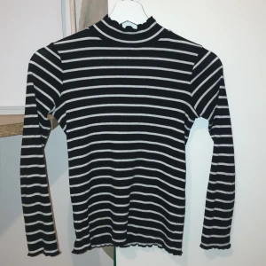 Svart och vit randig tröja från Lindex - Säljer en svart och vit randig tröja från Lindex Kids. Tröjan har långa ärmar och en hög krage med en liten volangdetalj. Perfekt för kyligare dagar! Storlek 134-140