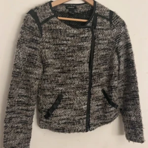 Gråmelerad jacka från Lindex - Snygg gråmelerad jacka från Lindex med dragkedja och svarta detaljer. Jackan har en modern look med långärmade ärmar och en stilren design. Perfekt för att ge din outfit en trendig touch.