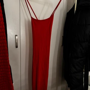 Röd axelbandslös klänning - Snygg röd klänning med smala axelband och en elegant, lång design. Perfekt för en kväll ute eller en speciell tillställning. Klänningen har en enkel och stilren look som framhäver figuren.