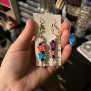 Färgglada fjärilsörhängen - ‼️gratis gåva får man alltid med‼️Unika örhängen med färgglada fjärilar i rött, blått och lila. De har även genomskinliga och blå pärlor som ger en lekfull touch. Perfekta för att liva upp vilken outfit som helst!