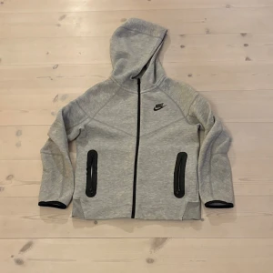 Grå nike tech - En grå Nike tech. Den har väldigt bra skick och har används 2-4 gånger. Jag säljer den för att den inte passar längre och därför har jag ingen användning av den. Den håller värmen och gör att använda på vintern och sommaren. Storleken är för 137-147 cm. 
