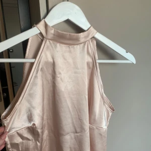 Beige halterneck topp - Snygg beige/ roséfärgad ärmlös topp i satin med hög hals och knytning i nacken. Perfekt för en elegant look. 