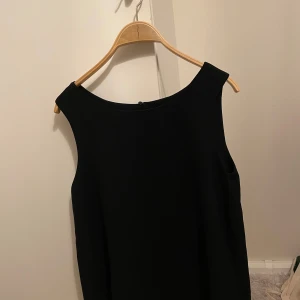 Svart klänning från Object - Elegant svart klänning från Object med en stilren design. Klänningen har en ärmlös stil och en klassisk rund halsringning. Perfekt för en minimalistisk look. Samt öppen rygg.