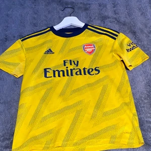 Arsenal bortatröja 2019/20 - En mycket fin Arsenal tröja från säsongen 2019/20 med Aubameyang på ryggen. Tröjan är 100% äkta och i väldigt bra skick. Säljer pga för liten, kontakta mig vid frågor eller närmare bilder på tröjan. Nypris 699kr