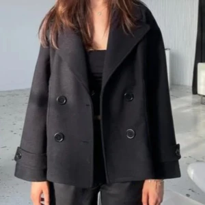 Svart kappa med knappar - Säljer en stilren svart kappa med stora knappar framtill. Den har en klassisk design med breda slag och långa ärmar. Perfekt för höst och vinter, och funkar både till vardags och fest. Passar bra över en tröja eller klänning.