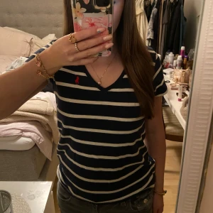 Randig t-shirt från Ralph Lauren Sport - Säljer en snygg randig t-shirt från Ralph Lauren Sport i marinblått och vitt. Den är gjord av 100% bomull och har en v-ringad hals. Använd fåtal gånger och inga defekter!💕