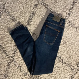 Nudie Jeans Grim Tim - Ett par mörkblå Nudie Jeans i storlek 29/32. Väldigt bra skick förutom en liten repskada vid gylfen. Modellen är Grimlund Tim