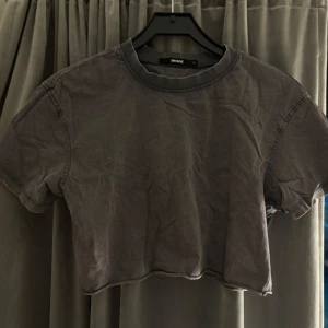 Grå croppad t-shirt från Bik Bok - Säljer en grå croppad t-shirt från Bik Bok i storlek S. Den är perfekt för en avslappnad stil och har korta ärmar. T-shirten är i bra skick och passar perfekt till baggy jeans eller kjol, med ett linne under eller till ett par mjukisbyxor hemma!