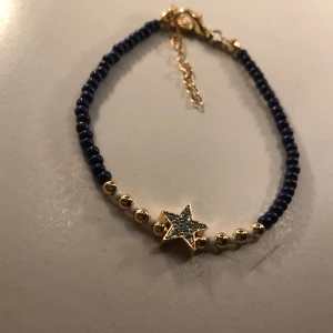 Armband - Säljer ett snyggt armband med mörkblå pärlor och en guldig stjärna i mitten. Stjärnan har små blå detaljer som ger en extra touch. Perfekt för att piffa upp vilken outfit som helst! ✨
