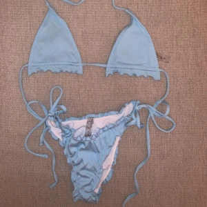 Ljusblå ribbad bikini - Säljer en superfin ljusblå bikini i ribbat material. Den har en söt volangdetalj längs kanterna och knytband både på överdelen och underdelen, vilket gör att storleken går att justera. Aldrig använd 