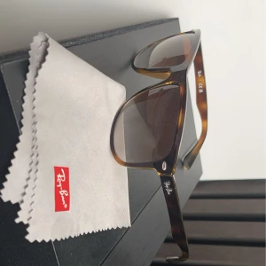 Bruna solglasögon från Ray-Ban - Säljer ett par snygga bruna solglasögon från Ray-Ban boyfriend. De har en klassisk design med sköldpaddsmönster på bågarna och mörka linser. Perfekta för både soliga dagar och som en stilren accessoar. Kommer med originalputsduk och fodral.