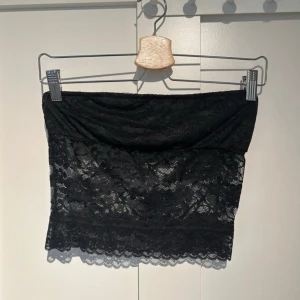Svart spets tubtopp - Säljer en snygg svart tubtopp i spets. Perfekt för festliga tillfällen! Toppen är axelbandslös och har en vacker spetsdetalj som ger en elegant touch. Passar bra till både kjol och byxor.