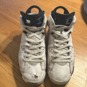Vita Nike Air Jordans i välanvänt skick - Säljer ett par vita Nike Air Jordans som har sett bättre dagar. De är i välanvänt skick med tydliga tecken på slitage, inklusive en reva på ena skon. Perfekta för någon som vill ha ett par sneakers med karaktär eller för ett DIY-projekt. Skorna har klassisk snörning och den ikoniska Jumpman-loggan på hälen.
