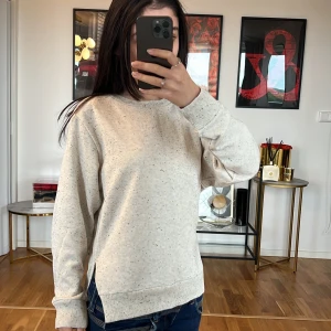 Beige sweatshirt JS - Säljer en supermysig beige sweatshirt i normal passform. Den är perfekt för både höst och vår, med långa ärmar och ribbade muddar vid ärmslut och nederkant. Den har små prickar i tyget som ger en extra touch. Perfekt för en avslappnad stil!
