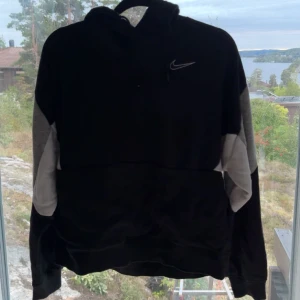 Svart och grå hoodie från Nike - Säljer en snygg och bekväm svart hoodie från Nike med grå detaljer på ärmarna. Den har en klassisk Nike-logga på bröstet och justerbara snören i huvan. Perfekt för höst och vinter, och passar både till vardags och träning.