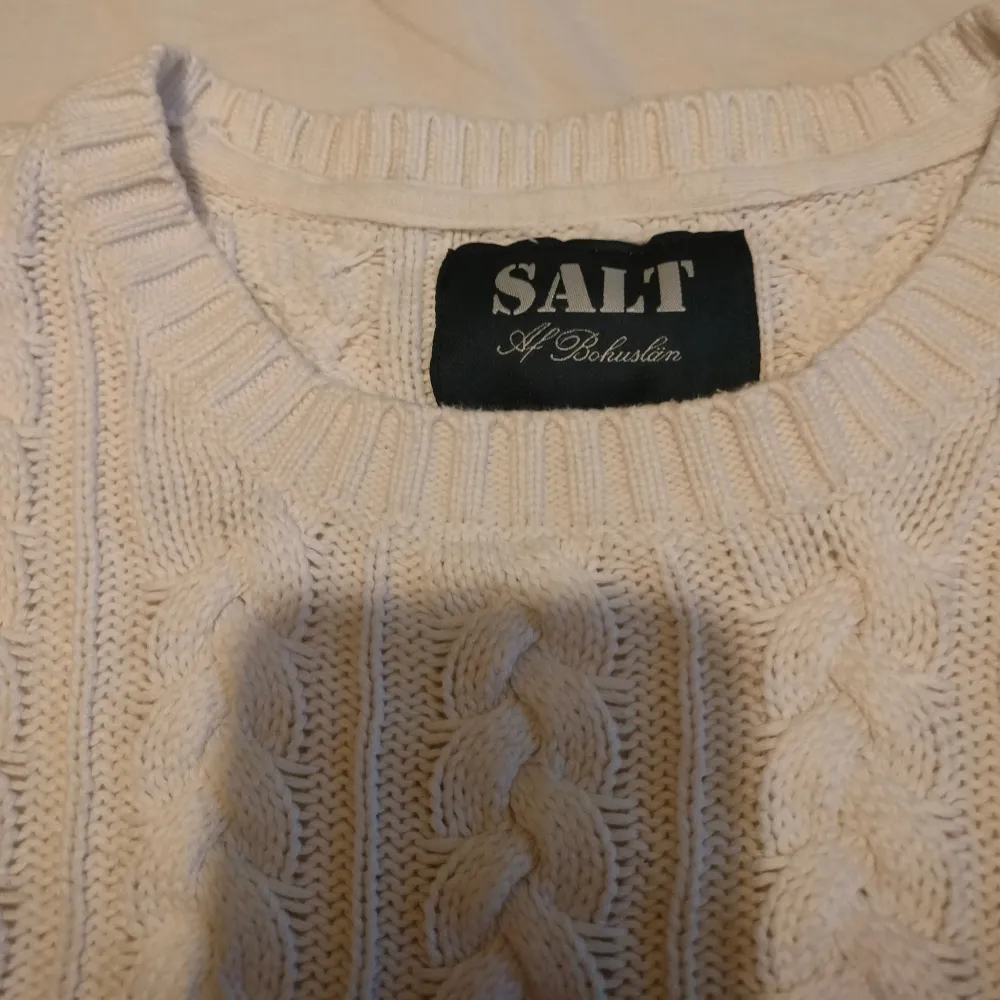 superfin vit stickad tröja från SALT. Den har ett klassiskt flätmönster och är perfekt för både höst och vinter. Tröjan är långärmad och har en ribbad kant vid ärmslut och nederkant. Perfekt för att hålla sig varm och stilren! Är mer som en S/M. Tröjor & Koftor.