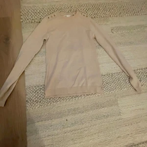 Beige tröja med knappar - Säljer en stilren beige tröja med långa ärmar och knappar på axlarna. Perfekt för höst och vår, den är både bekväm och snygg. Passar bra till både jeans och kjol!