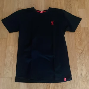 Liverpool FC T-shirt svart - Säljer en stilren Liverpool T-shirt. Passar för en clean och avslappnad stil.