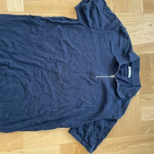 Mörkblå t-shirt med dragkedja från Zara - Säljer en mörkblå pike från Zara med en dragkedja framtill. Den är kortärmad och perfekt för en avslappnad stil. Materialet känns mjukt och bekvämt, perfekt för vardagsbruk.
