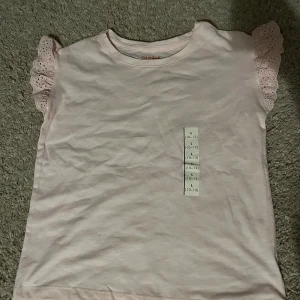 Ljusrosa topp med spetsärmar - Söt ljusrosa topp med korta spetsärmar. Perfekt för sommarens varma dagar. Toppen har en enkel design med en liten volang. storlek L men kidsize så sitter som en Xs/s