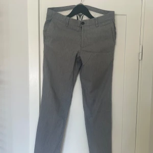 Grå kostymbyxor från Riley - Säljer ett par stiliga grå kostymbyxor från Riley. De har en klassisk design med knappar och fickor både fram och bak. Perfekta för både kontoret och mer formella tillfällen. Byxorna är i bra skick och redo för en ny ägare!