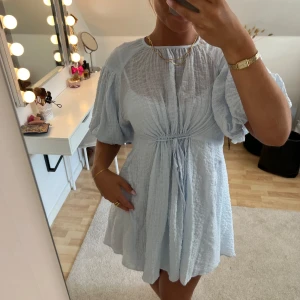 Ljusblå miniklänning - Supergullig ljusblå miniklänning i fluffigt mjukt och lyxigt tyg. Lite längre baktill. Knyts med snören framtill och baktill. Har inneklänning. Storlek S. Är 167 cm lång och vanlig S-M. Knappt använd.