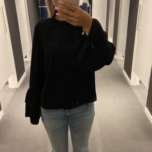 Svart långärmad tröja med volangdetaljer - Säljer en superfin svart tröja med långa ärmar och volangdetaljer vid ärmsluten. Den har en hög krage med en liten volangkant som ger en söt touch. Perfekt för höst och vinter, och funkar både till vardags och fest. Materialet känns mjukt och bekvämt. Passar perfekt till jeans eller kjol!