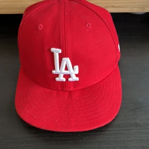 Röd keps från New Era - Säljer en snygg röd keps från New Era med LA-logga framtill. Kepsen är i modellen 59FIFTY och har en broderad MLB-logga baktill. Perfekt för att ge din outfit en sportig touch!