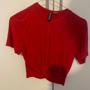 Röd kortärmad topp från Divided - Säljer en snygg röd kortärmad topp från Divided. Den är croppad och har en knutdetalj framtill som ger en cool look. Perfekt för sommardagar eller en avslappnad festkväll!