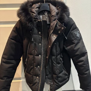 Svart vinterjacka från Horspist Paris - Snygg svart pufferjacka från Horspist med avtagbar päls på huvan. Helt slutsåld överallt och säljs inte längre. Nypris 6900kr. Jackan har dragkedja och knappar framtill samt en broderad logotyp på ärmen. Perfekt för kalla dagar med sin quiltade design.