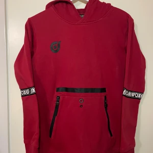 Röd hoodie  - Säljer en cool röd hoodie  med svarta detaljer och dragkedjor på fickorna. Tröjan har en stor huva och tryck på ärmarna. För barn i storlek 158/164