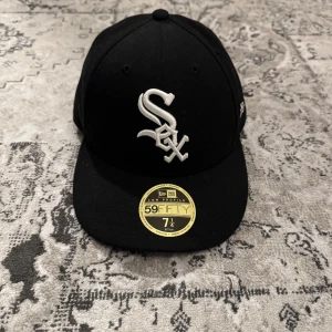 Svart keps från New Era - Snygg svart keps från New Era med broderad vit logotyp framtill. Klassisk 59FIFTY-modell med platt skärm och MLB-logga baktill. Perfekt för sportiga tillfällen eller som en stilren accessoar. Kepsen var en present och är använd ett fåtal gånger. Är öppen till att mötas upp i Stockholm.