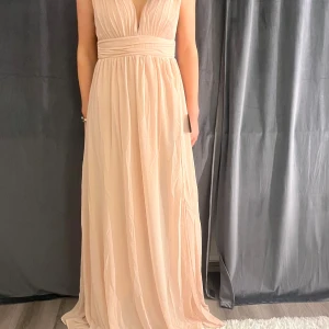 Rosa färgad långklänning med slits - Elegant rosa färgad långklänning med djup v-ringning och slits framtill. Klänningen har en omlott-design och är ärmlös. Perfekt för speciella tillfällen. Helt oanvänd endast testad med lappen på.