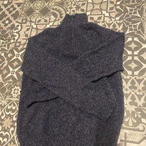 Mörkblå stickad tröja med dragkedja - Säljer en mörkblå stickad tröja med dragkedja i halsen. Tröjan har långa ärmar och är perfekt för kyligare dagar. Den är både stilren och bekväm.