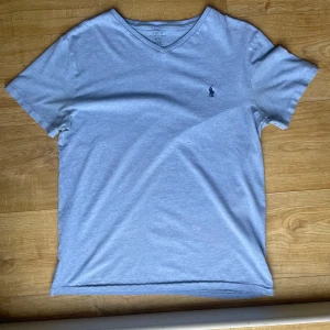 Grå v-ringad t-shirt från Polo Ralph Lauren - Snygg grå v-ringad t-shirt från Polo Ralph Lauren med det klassiska broderade logotypen på bröstet. Perfekt för en stilren och avslappnad look. Tillverkad i mjukt bomullsmaterial för extra komfort.