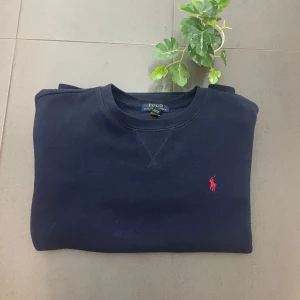 Mörkblå sweatshirt från Ralph Lauren - Säljer en stilren mörkblå sweatshirt från Ralph Lauren med det klassiska röda logotypbroderiet på bröstet. Tröjan är tillverkad i mjuk bomull och har långa ärmar samt ribbade muddar vid ärmslut och nederkant. Perfekt för en avslappnad stil.