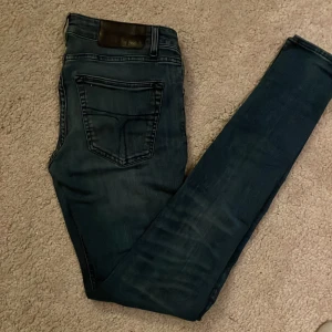 Blå jeans från Tiger of Sweden - Snygga blå jeans från Tiger of Sweden med en skinny passform. De har en klassisk femficksdesign och en knappgylf. Perfekta för en stilren look. De är i storlek w26 l30. Hör av er vid frågor eller funderingar.