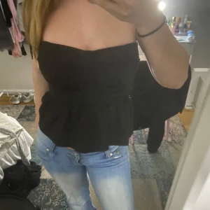 Svart tubtopp - Snygg svart tubtopp med en peplumdetalj som ger en fin siluett. Perfekt för en stilren look och kan enkelt matchas med jeans eller kjol.