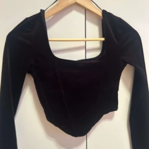 Svart sammetstopp - Elegant svart sammetstopp med långärmad design och fyrkantig halsringning. Perfekt för en stilren look.