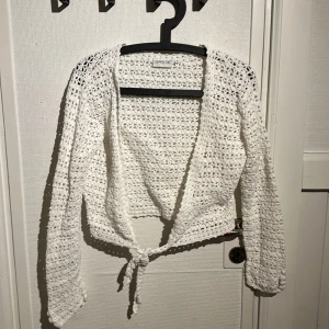 Vit stickad kofta från Cappuccino - Säljer en söt vit stickad kofta från Cappuccino. Den har en knytning framtill och långa ärmar. Perfekt för en avslappnad stil. Passar bra till både jeans och kjol. 🧶✨