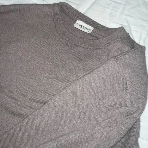 Beige stickad tröja från John Smedley - Säljer en stilren beige stickad tröja från John Smedley. Tröjan har en klassisk rund hals och långa ärmar, perfekt för kyligare dagar. Den är mjuk och bekväm, vilket gör den till ett utmärkt val för både vardag och mer avslappnade tillfällen.