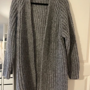 Grå stickad kofta från Zara - Mysig grå stickad kofta från Zara. Perfekt för kyliga dagar med sin långa design och bekväma passform. Koftan har en öppen front och långa ärmar, vilket gör den lätt att slänga på över vilken outfit som helst. Ett måste i garderoben för höst och vinter! 🍂❄️