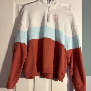 Flerfärgad tröja från Levi's - Säljer en snygg flerfärgad tröja från Levi's med dragkedja och hög krage. Tröjan har en färgblockdesign i vitt, ljusblått och rödbrunt. Den har långa ärmar och ett broderat Levi Strauss & Co. märke på bröstet. Perfekt för en avslappnad stil.