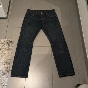 Levi's 501 jeans - Säljer ett par klassiska Levi's 501 jeans i mörkblå denim. Dessa jeans har en rak passform och är tillverkade av högkvalitativt denim. Perfekta för en tidlös stil. Levi's Premium-märke på insidan och den ikoniska röda etiketten på fickan.